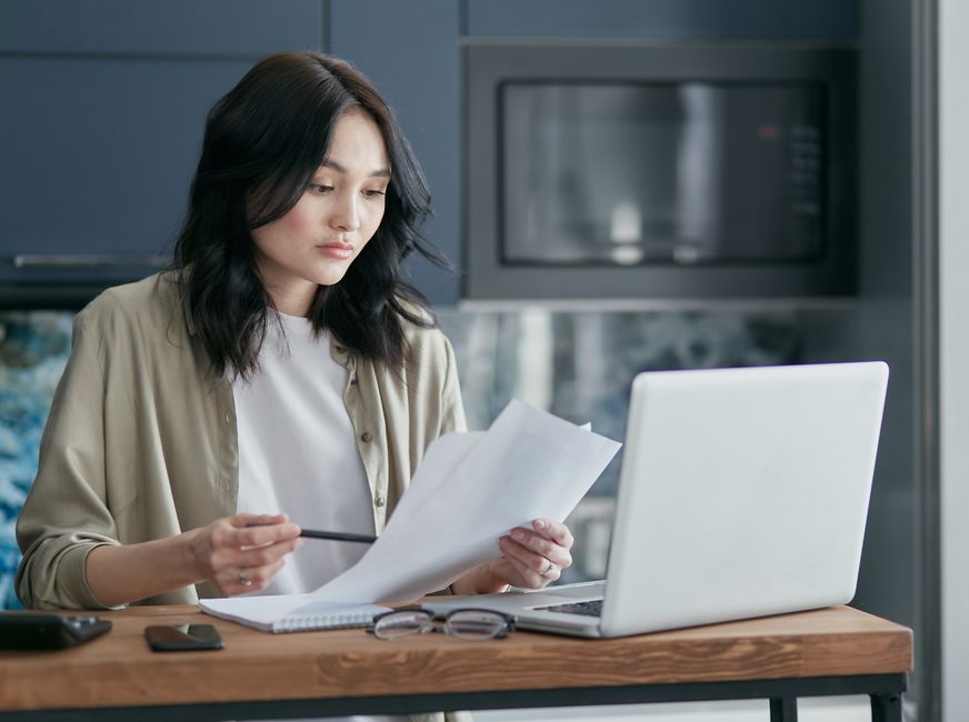 自宅の机で書類とパソコンに向かう女性
